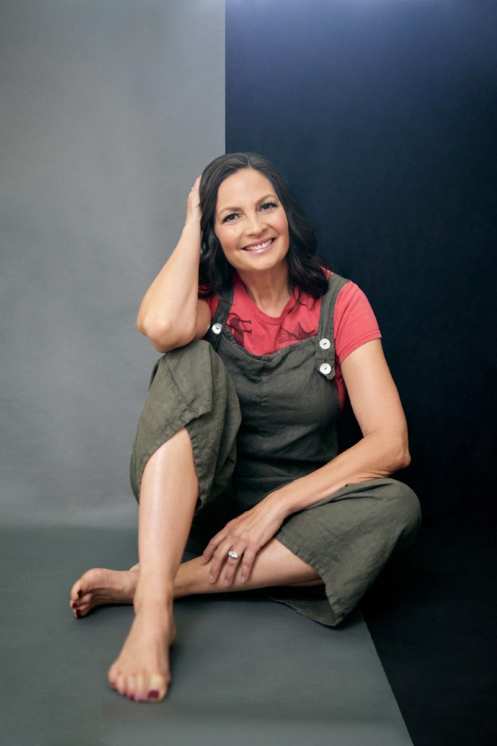 Naomi Simpson sitting cross-legged in a green jumper and smiling